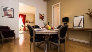 A dining area with a wooden table, four chairs, and a vase with flowers. There are framed pictures on the walls and a red curtain in the background. - Apartamento Deluxe de Tres Habitaciones (Barcelona)