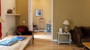 A living room with a red armchair, a wooden coffee table with books, a brown sofa, and a small white side table with a lamp. - Apartamento Deluxe de Tres Habitaciones (Barcelona)