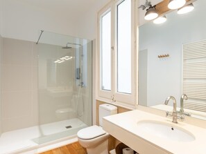 A modern bathroom with a glass-enclosed shower, a white toilet, a sink with a mirror, and a window. - Apartamento de Tres Habitaciones con Terraza 21B (Barcelona)