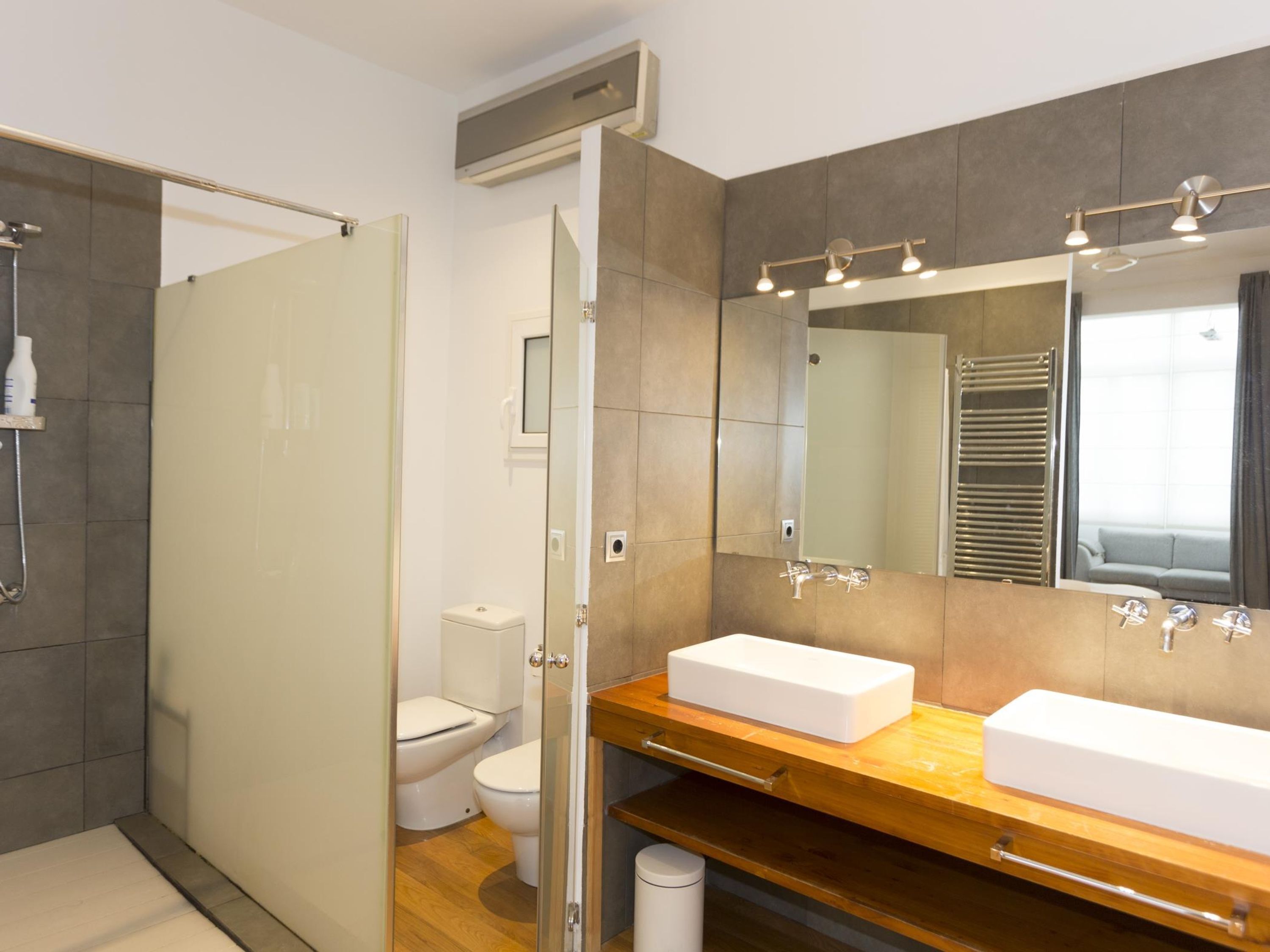 Un baño moderno con cabina de ducha de vidrio, dos lavamanos blancos, un espejo grande y un mueble de tocador de madera.