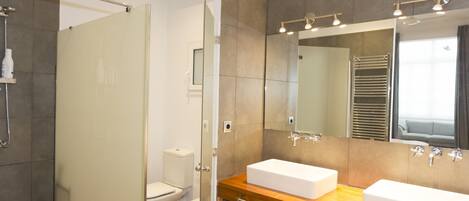 Un baño moderno con cabina de ducha de vidrio, dos lavamanos blancos, un espejo grande y un mueble de tocador de madera.