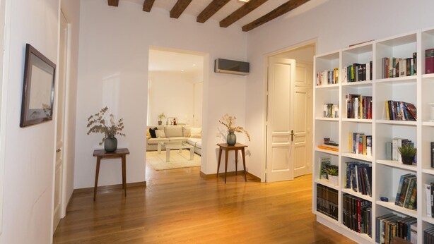 A spacious room with wooden beams on the ceiling, a bookshelf filled with books, and a cozy seating area with a sofa and coffee table. - Apartamento de Tres Habitaciones con Terraza 21B (Barcelona)