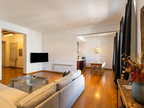 A modern living room with a sofa, a glass coffee table, a flat-screen TV, and a dining area with a wooden table and chairs. - Apartamento de Tres Habitaciones con Terraza 21B (Barcelona)