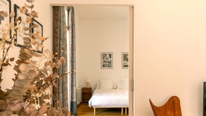 A bedroom with a bed, a nightstand, and a chair. There are framed pictures on the wall and a window with curtains. - Designer s Three Bedroom Apartment With Terrace (Barcelona)