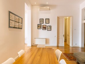 A modern dining room with a wooden table and white chairs, a radiator, and framed pictures on the wall. - Designer s Three Bedroom Apartment With Terrace (Barcelona)