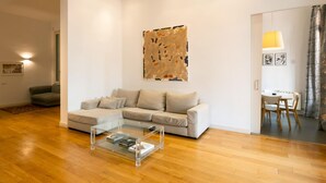 A modern living room with a glass coffee table, a beige sectional sofa, and a large abstract painting on the wall. - Designer s Three Bedroom Apartment With Terrace (Barcelona)