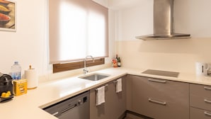 A modern kitchen with a dishwasher, sink, and stainless steel range hood. - Apartamento Tico con Terraza (Barcelona)