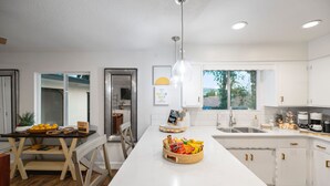 Una cuina moderna amb armaris blancs, una illa central i una zona de menjador amb taula i cadires.