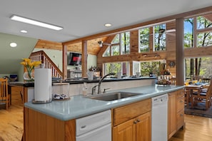 A spacious kitchen with wooden beams, a large island with a sink, and a dining area with a view of trees.