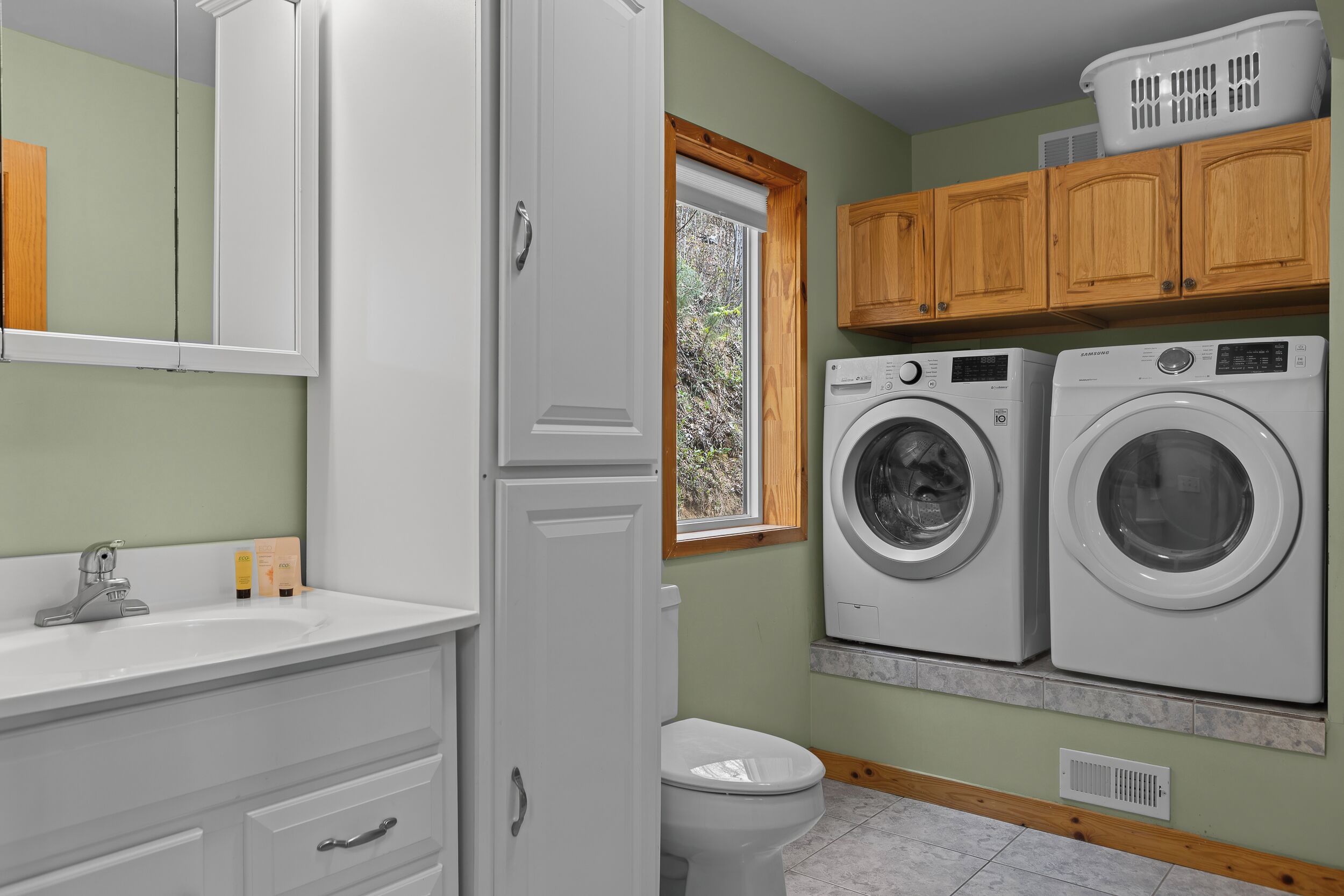 A laundry room with two front-loading washing machines, a white sink, and wooden cabinets.
