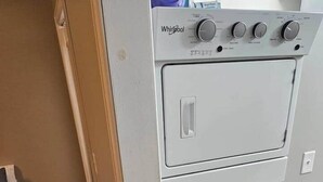 Eine kompakte, weiße Whirlpool Wasch- und Trockner-Kombination in einem kleinen Raum mit Holzboden und einer braunen Wand.
