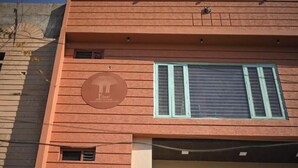 Un bâtiment à la façade marron, orné d’un logo circulaire représentant un bâtiment, et doté d’une grande fenêtre avec des volets verts.