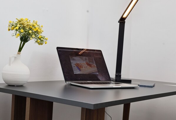 A laptop on a desk with a white vase of yellow flowers and a black desk lamp.