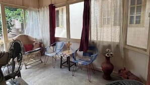 Une pièce avec un ventilateur, deux tables avec des chaises, un vase décoratif et une fenêtre avec des rideaux.