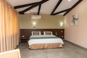 A hotel room with a bed, curtains, an air conditioning unit, a nightstand, and a painting on the wall. - CRESPOTEL (Quevedo)