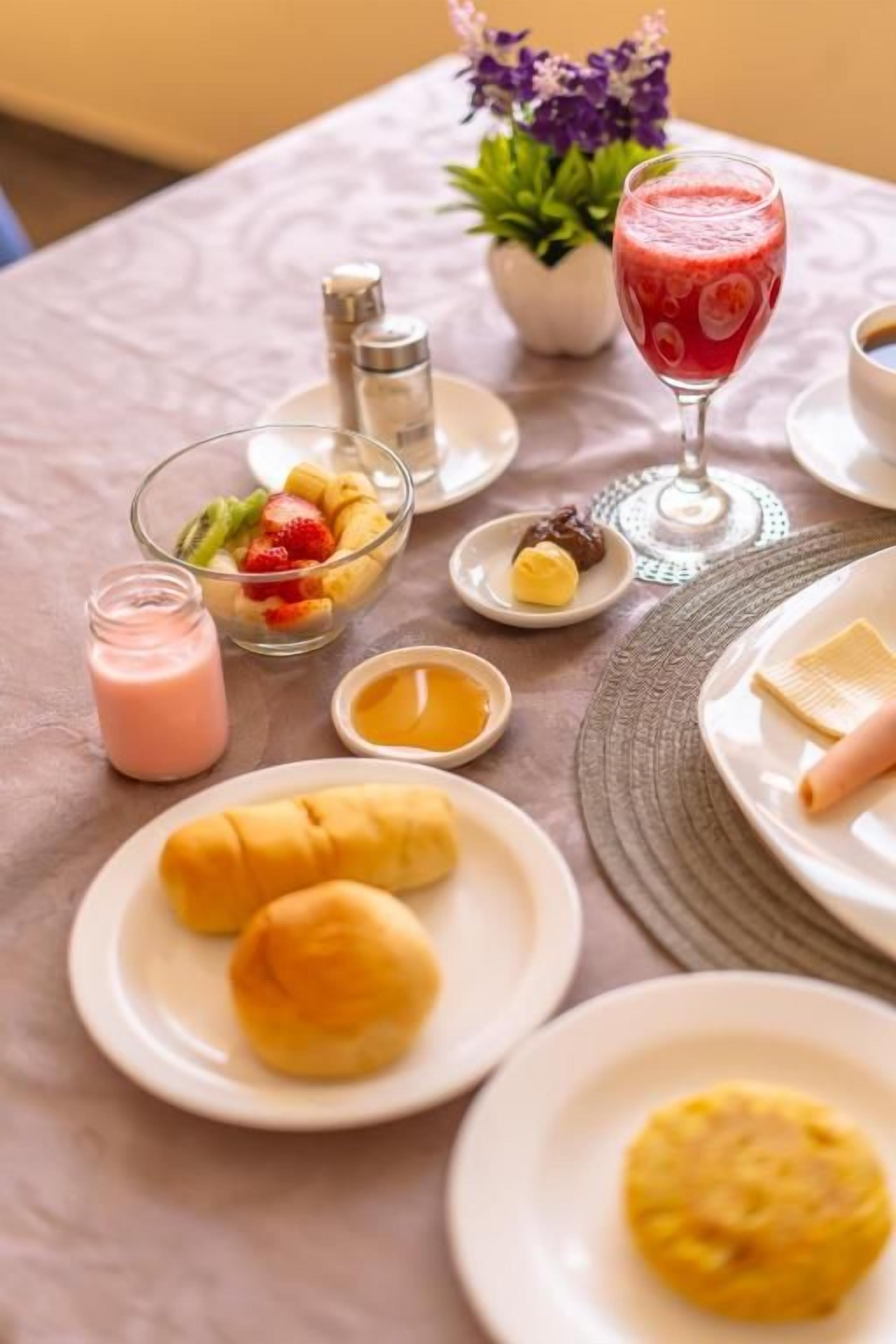 A breakfast setting with croissants, a fruit bowl, a glass of red juice, and a candle on a table.