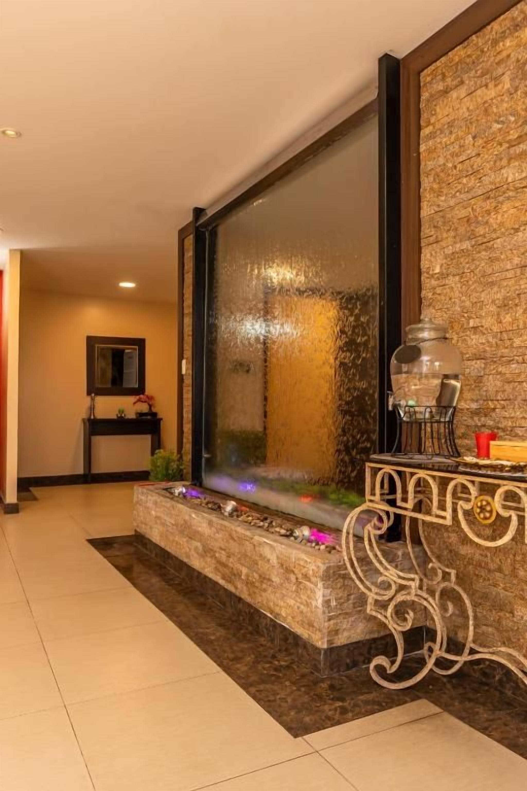 Un interno moderno con una fontana decorativa, un pannello di vetro e un tavolo in metallo con un vaso.