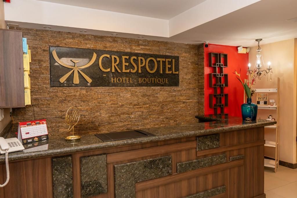 Una recepción de hotel con un cartel que dice 'CRESPOTEL HOTEL BOUTIQUE', un calendario, un teléfono y un emblema decorativo.