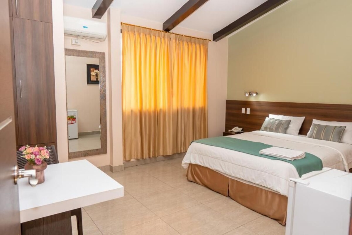 A hotel room with a bed, bedside table, and a mirror.