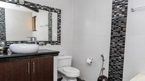 Uma casa de banho moderna com uma sanita branca, lavatório e bidé, um espelho grande e área de duche revestida a azulejos.