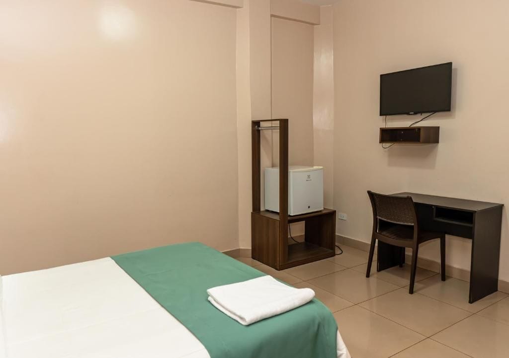 Una camera d'albergo con un letto, una scrivania, una sedia, una televisione e uno specchio.