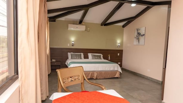 Quarto de hotel com cama, poltrona, ar condicionado e um quadro na parede.
