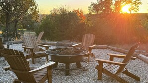 A circular fire pit surrounded by wooden Adirondack chairs on a gravel surface. - Cabin 1 of 4 comfortably nestled in a country setting with amazing sunset view (Weatherford)