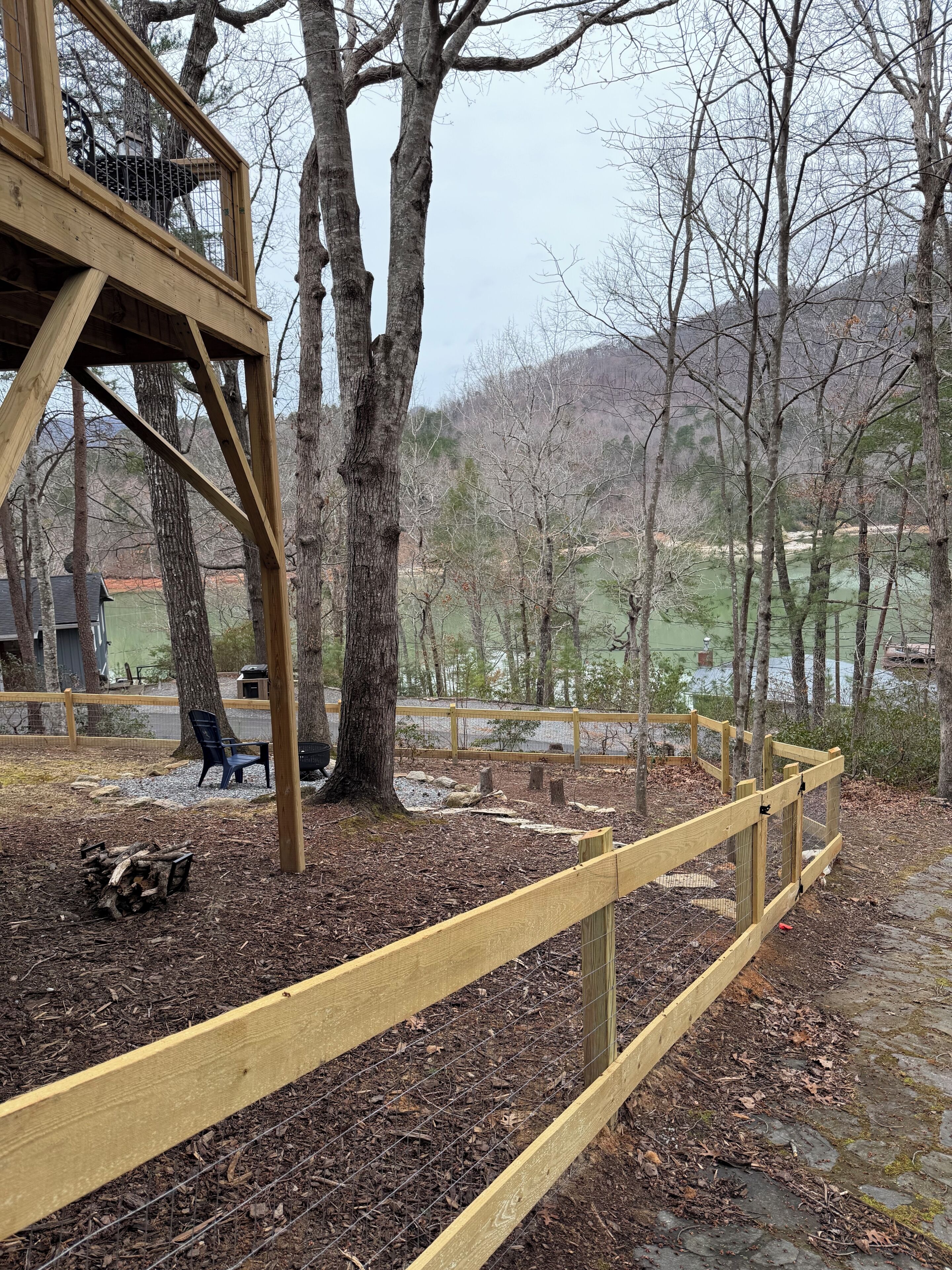 Une terrasse en bois avec une rambarde en métal, entourée d’arbres et offrant une vue sur un lac.