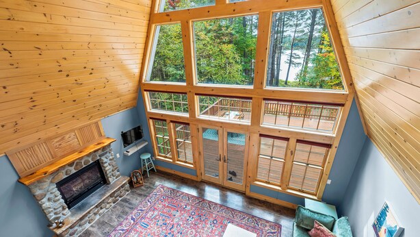 A spacious room with a large window, a stone fireplace, and a colorful rug.