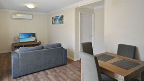 Ein Wohnzimmer mit grauem Sofa, einem Holztisch und einem Fernseher, der eine Strandansicht zeigt.