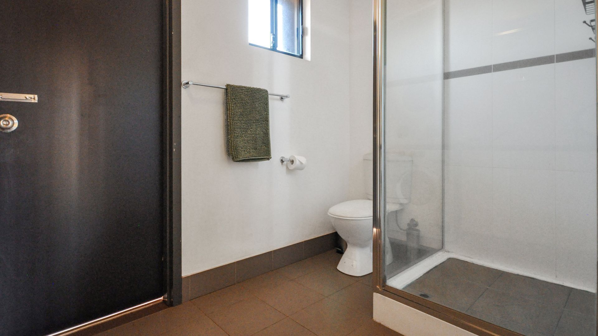 Ein Badezimmer mit Toilette, einem Handtuch auf einem Halter und einer Duschkabine aus Glas.