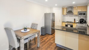 A compact kitchen with a dining area, featuring a refrigerator, microwave, stove, and a small trash bin. - Pilbara Chalet Private 1x1 (Port Hedland)