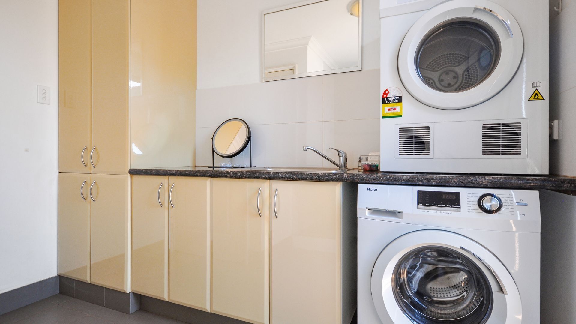A compact laundry area with a front-loading washer and dryer, a small mirror, and a cabinet with a mirror above it.