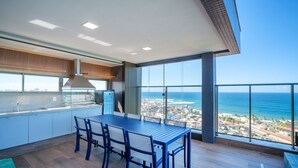 A modern kitchen with a large island, a dining area with a table and chairs, and a balcony with a view of the ocean and cityscape. - Apartments in a Building With a Pool 800m From the Beach in Salvador - EDF (Salvador)
