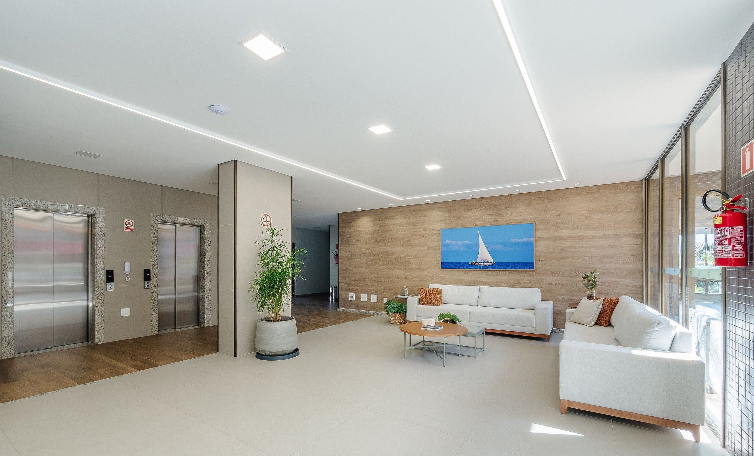 Un hall d’entrée moderne avec un comptoir d’accueil, un canapé blanc, un tableau représentant un voilier et un ascenseur.