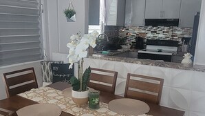 Un comedor con una mesa de madera dispuesta para seis personas, rodeada de sillas. Un orquídeo en maceta está sobre la mesa, y hay dos espejos montados en la pared encima.