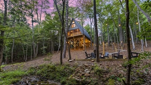 A cabin in a forest with a stream, surrounded by trees and outdoor seating. - Creekside • Sauna • Hot Tub • Fire Pit • 15 min to Town (Morganton)