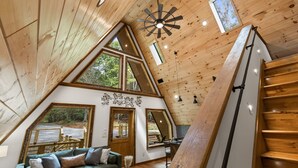 A cozy, wooden interior with a sloped ceiling, large windows, and a staircase. - Creekside • Sauna • Hot Tub • Fire Pit • 15 min to Town (Morganton)