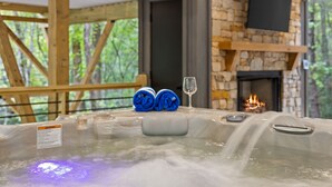 A hot tub with a warning label, a glass of wine, and a stone fireplace in the background. - Creekside • Sauna • Hot Tub • Fire Pit • 15 min to Town (Morganton)