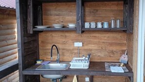 A compact kitchen with a sink, a dish rack, and shelves above for storage. - Brown Bosnian pyramid glamping (Visoko)