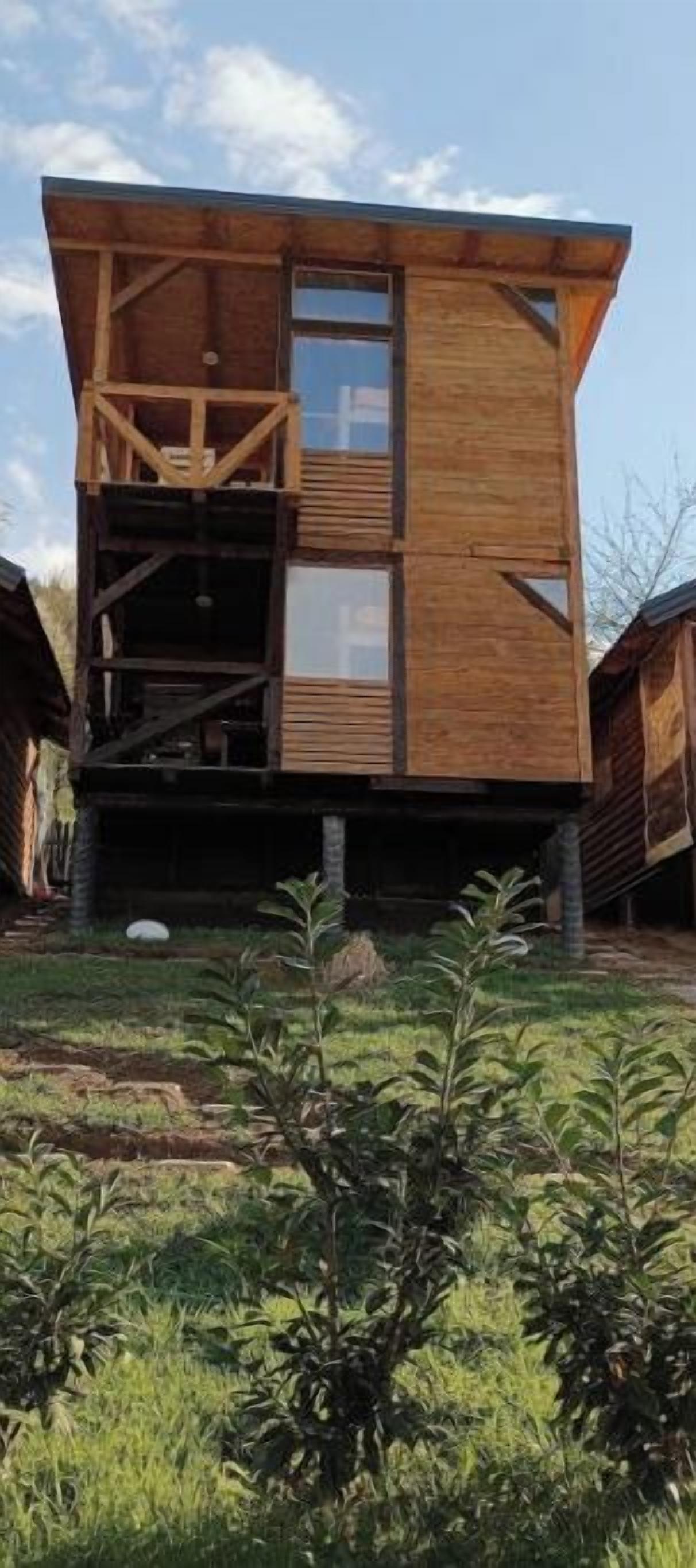 Une cabane en bois dotée d’un balcon, d’une grande fenêtre et d’un petit jardin.