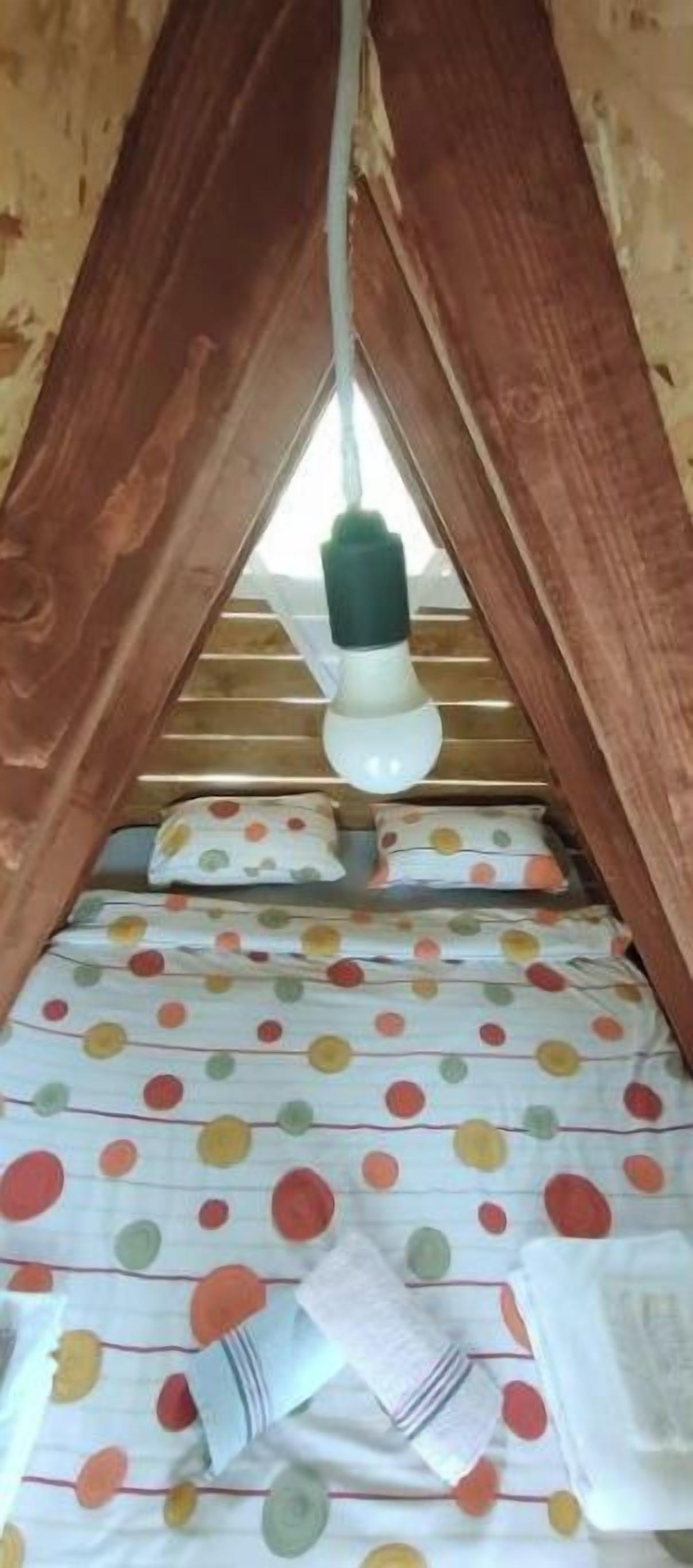 A small attic bedroom with a sloped ceiling, a single light bulb hanging from the center, and a polka dot bedspread.