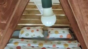 A small attic bedroom with a sloped ceiling, a single light bulb hanging from the center, and a polka dot bedspread.