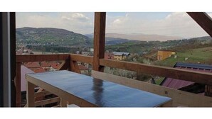A wooden balcony with a view of a hilly landscape and buildings in the distance. - White Bosnian pyramid glamping (Visoko)