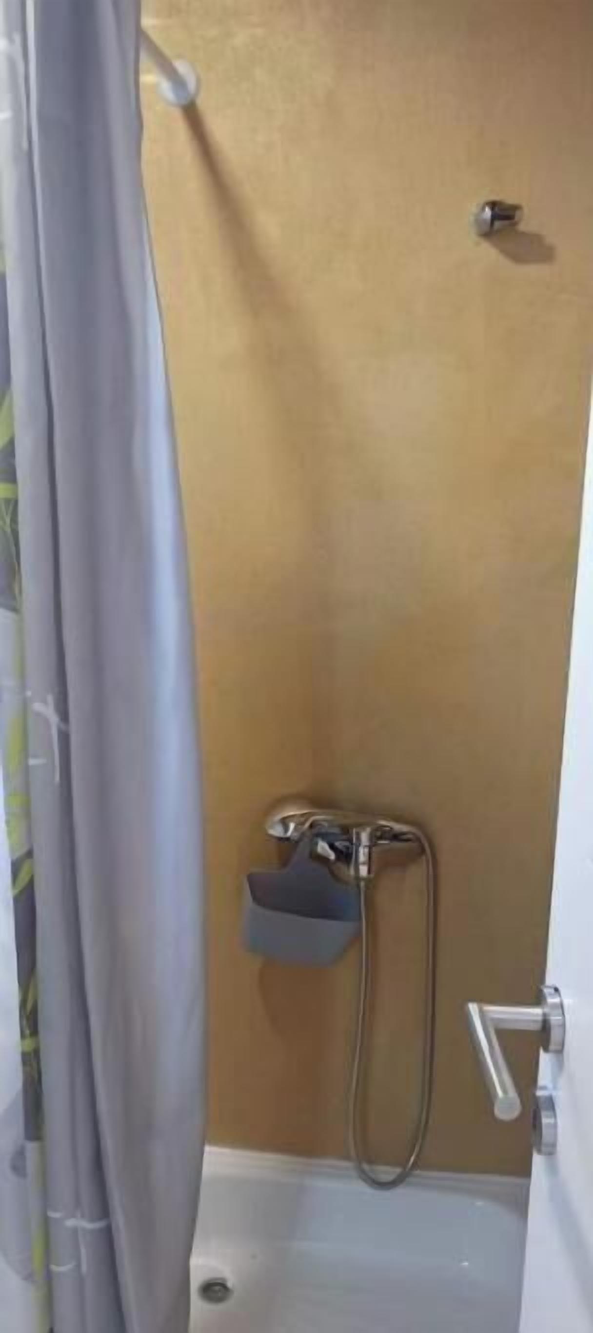 A small bathroom with a shower, a towel rack, and a door handle.