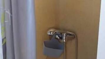 A small bathroom with a shower, a towel rack, and a door handle.