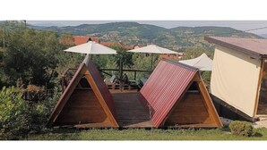 Two wooden A-frame tents with white canopies, set on a wooden deck with a view of a hilly landscape. - Dragon Tent Bos pyramid glamping (Visoko)