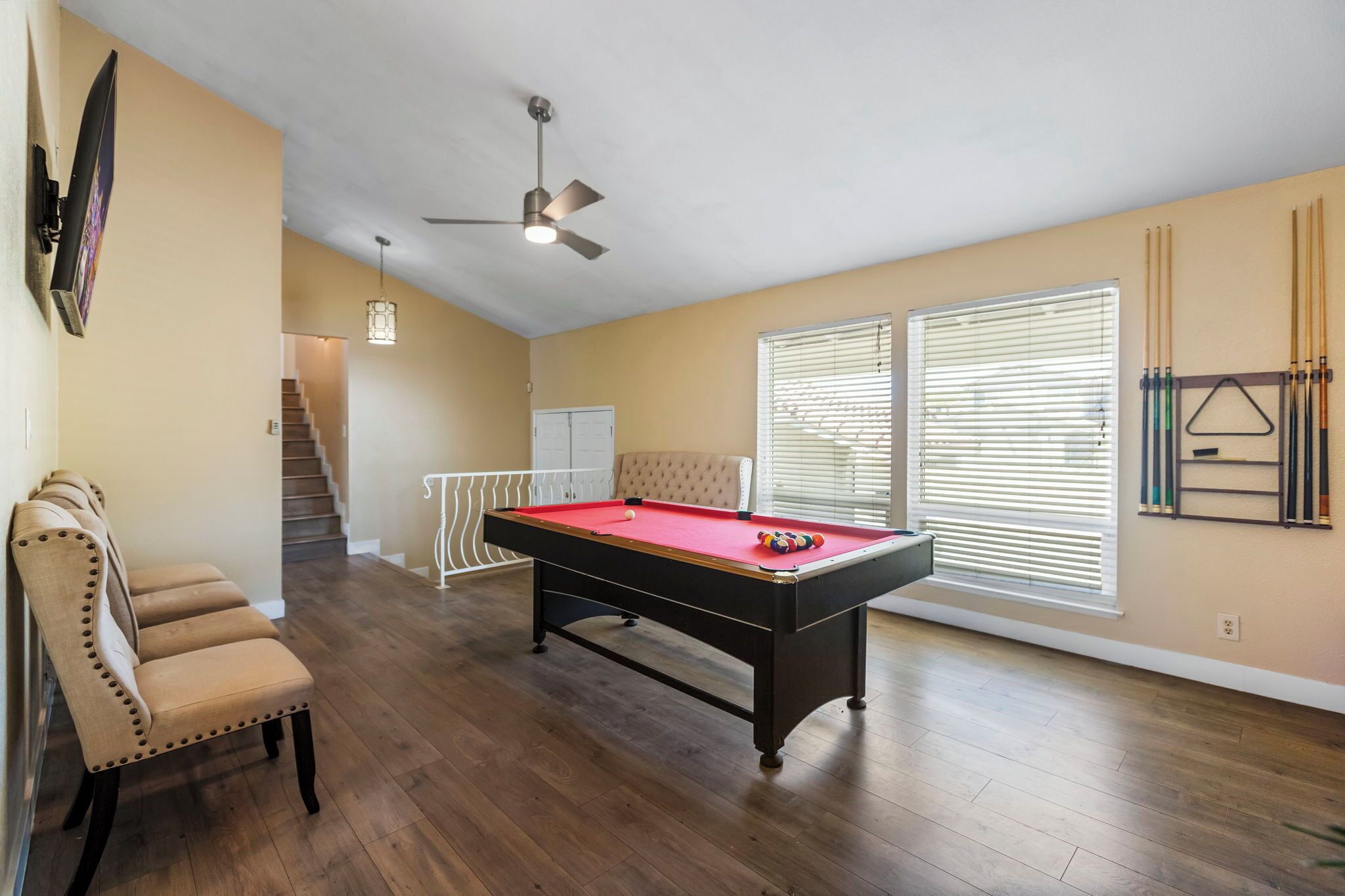 A spacious room with a pool table, a ceiling fan, and a staircase leading to another level.