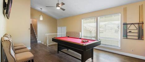 A spacious room with a pool table, a ceiling fan, and a staircase leading to another level.