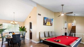 Een pooltafel in een ruimte met een eethoek, een trap en een plafondventilator.